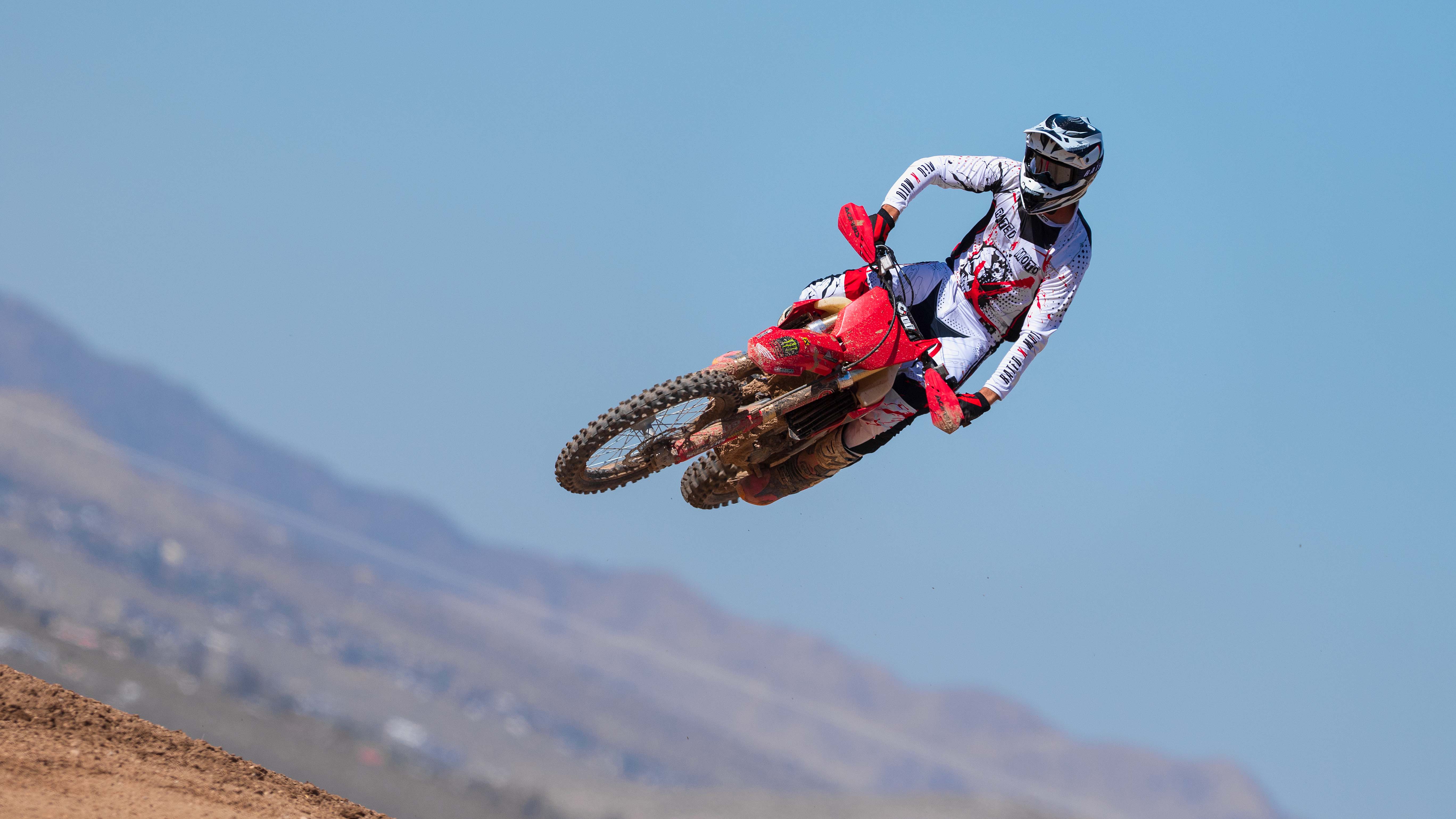 Motocross rider performing a jump on a dirt bike against a clear blue sky.